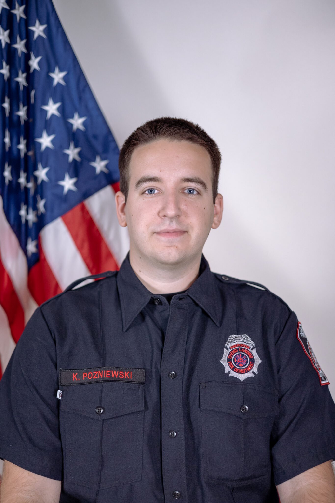 A firefighter posing in uniform in front of an American flag.