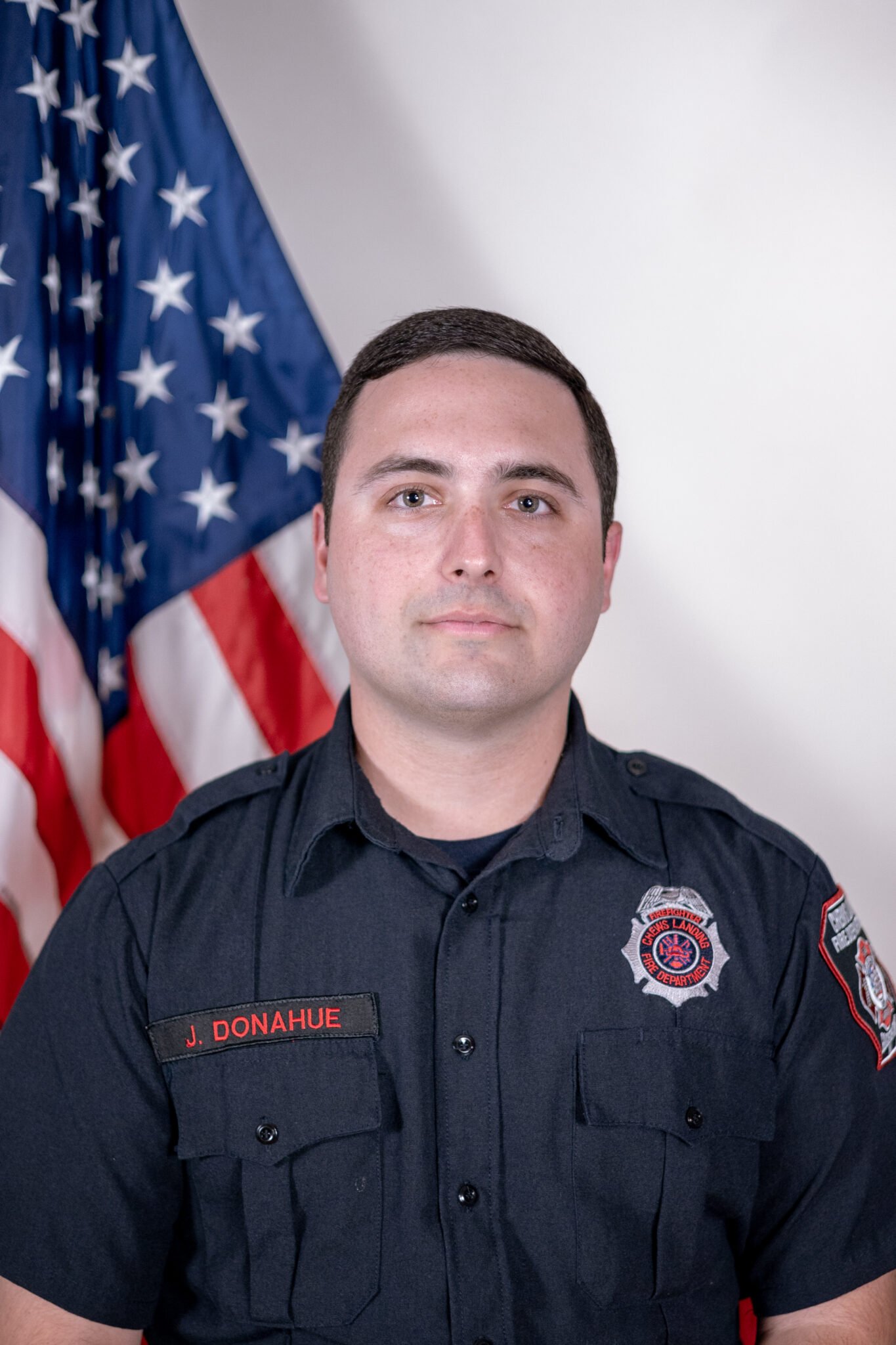 A firefighter posing in uniform in front of an American flag.